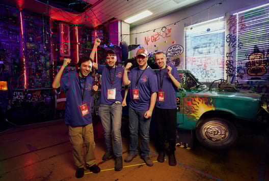 A full team in blue shirts is posing with big smiles and raised fists to celebrate their success.