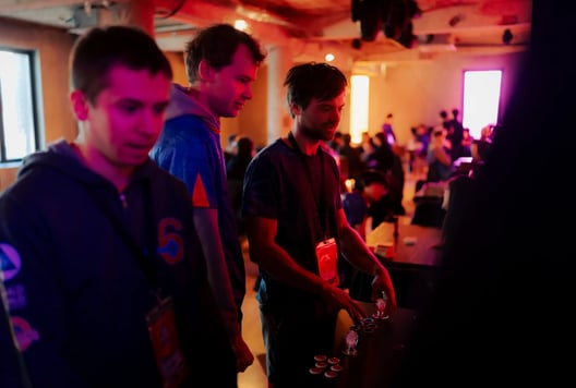 Three participants with badges examine a game station.