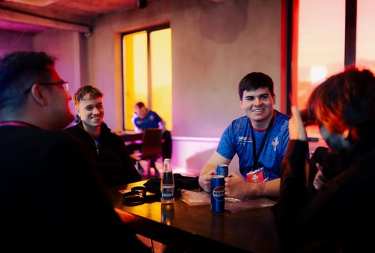 A group of young people sit at a table, talking and laughing during a break.