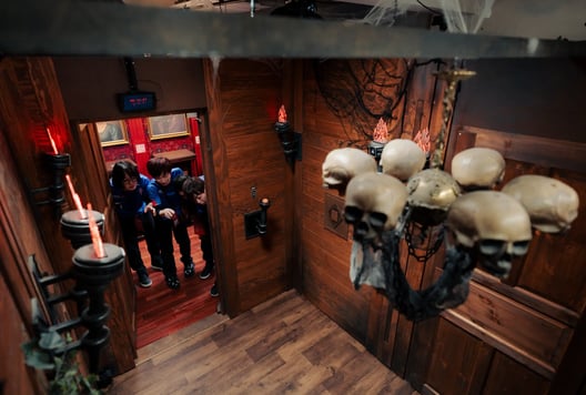 Three teammates cautiously enter a spooky, skull-decorated escape-room chamber.