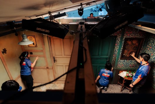 Players examine different puzzles across adjoining rooms while a game master watches from above.