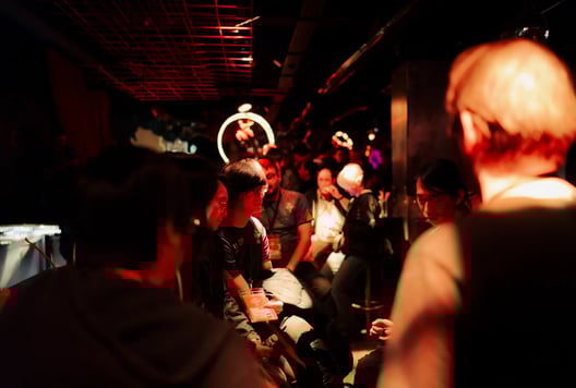 Participants chat closely in a dim, warm-lit lounge full of people.