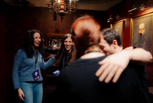 A group of friends share a joyful hug and laughter inside an escape-room environment.
