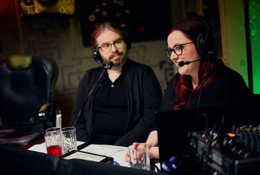 Two commentators with headsets are sitting at a desk and talking during the event.